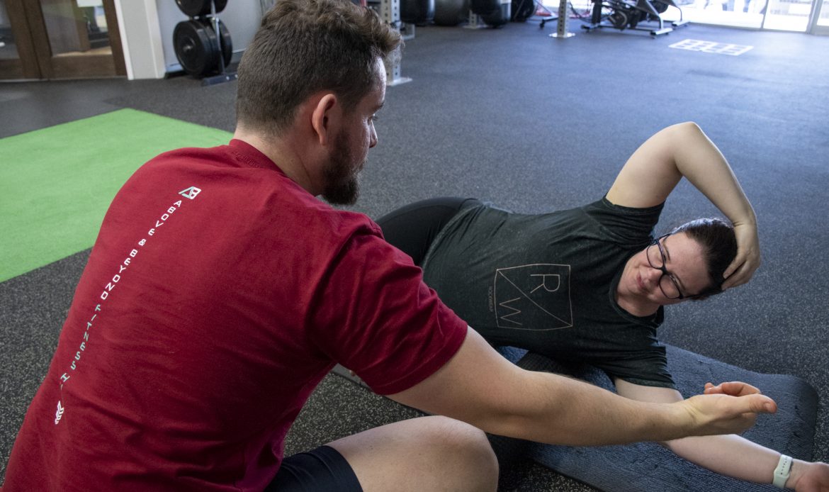 Photo of a trainer showing a client an exercise | Featured Image for Stretch & Recover Classes Page by AB Fitness Hub.